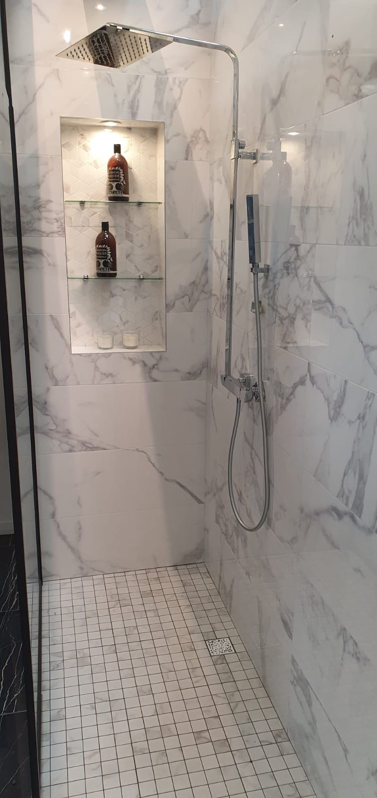 Douche à l'italienne carrelée en marbre blanc Calacatta, avec niche et sol mosaïque